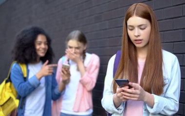 Bullied female student reading embarrassing news social networks by smartphone